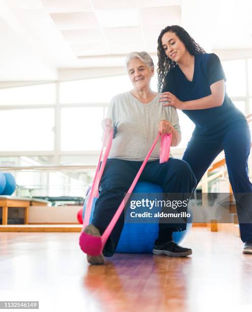 senior woman stretching leg with exercise band - senior physiotherapy stock pictures, royalty-free photos & images