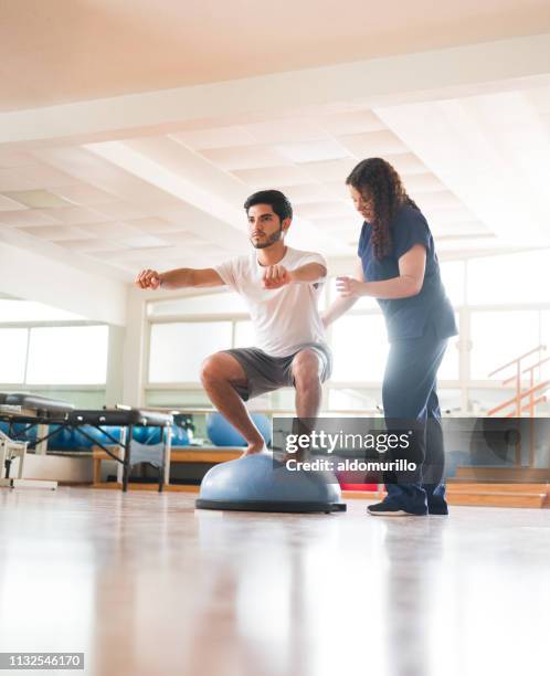 young latin man squatting on bosu ball next to physical therapist - sports physiotherapy stock pictures, royalty-free photos & images