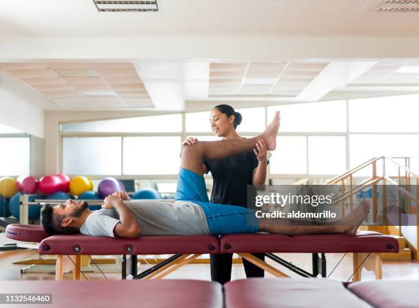 mannelijke patiënt liggend op massagetafel met been gehouden door massage therapeut - latina legs stockfoto's en -beelden