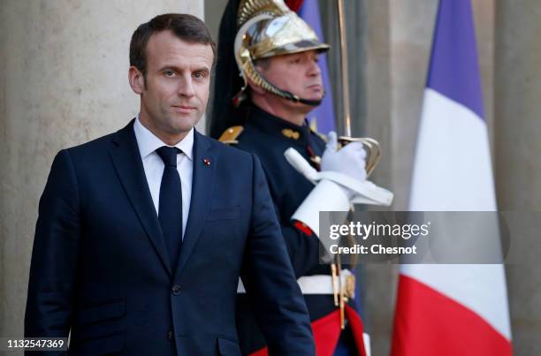 French President Emmanuel Macron waits as German Chancellor Angela Merkel leaves the Elysee Presidential Palace after their meeting on February 27,...