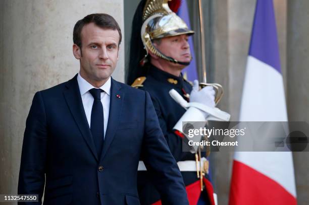 French President Emmanuel Macron waits as German Chancellor Angela Merkel leaves the Elysee Presidential Palace after their meeting on February 27,...