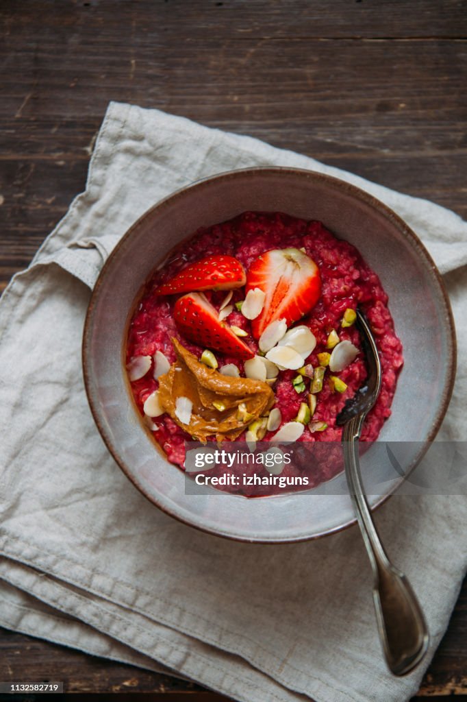 Oatmeal porridge with strawberries and fruit yogurt and pistachios, peanut butter and almond in bowl. Morning concept with copy space