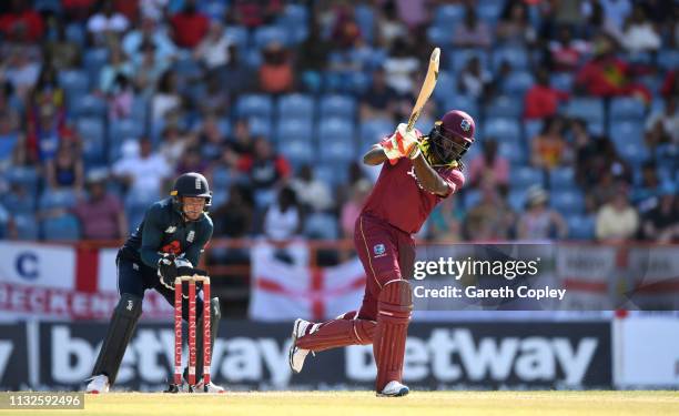 Chris Gayle of the West Indies hits out for six runs watched by England wicketkeeper Jos Buttler during the 4th One Day International match between...