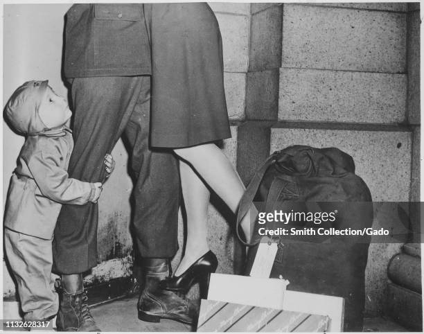 Young boy clutches the leg of his father, a soldier who was able to go home for the holidays, who lifts his wife off the ground, 1944. Image courtesy...