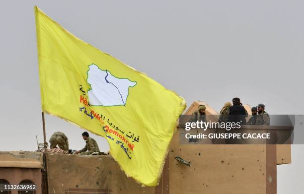 Fighters of the Syrian Democratic Forces stand atop a roof next to their unfurled flag at a position in the village of Baghouz in Syria's eastern...