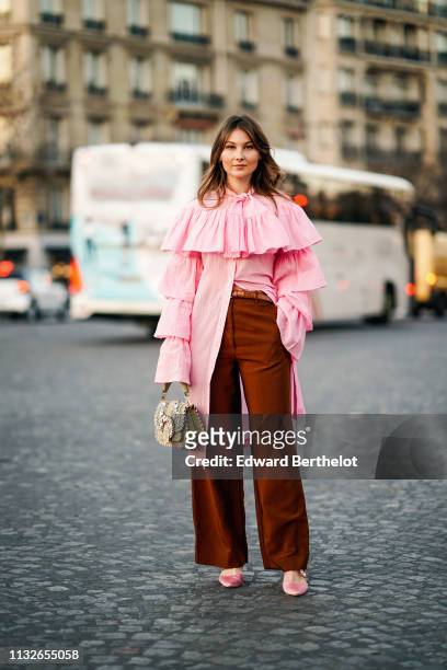 Angelica Ardasheva wears a pink ruffled long shirt, a bag with embroidery, brown flared pants, pink shoes, outside Rochas, during Paris Fashion Week...