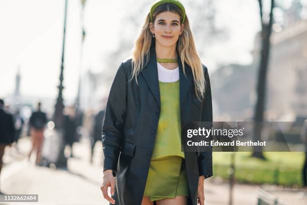 Veronika Heilbrunner wears a headband, a leather long jacket, a green dress, boots, outside Maison Margiela, during Paris Fashion Week Womenswear...