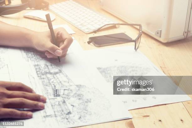 close-up hand of male architect drawing blueprint on work space wooden table in office - cad drawing stock pictures, royalty-free photos & images