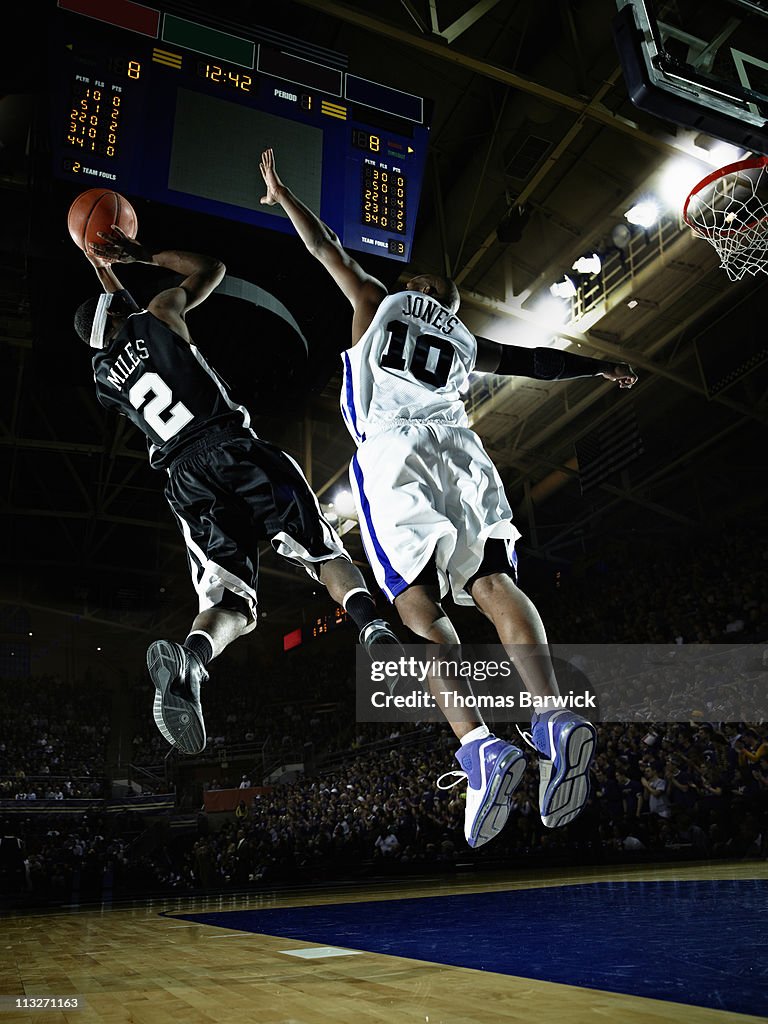 Basketball player shooting over defender in arena