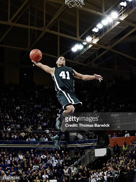 basketball player preparing to dunk ball in arena - basketball stock-fotos und bilder