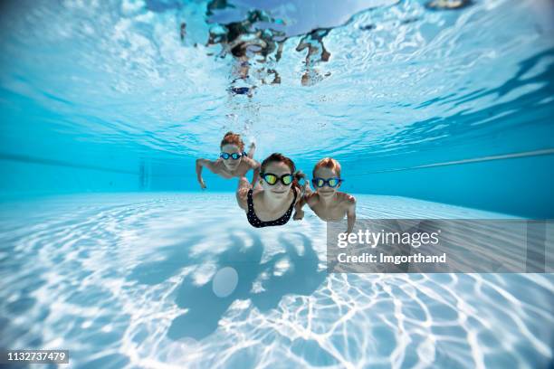 tres niños felices nadando bajo el agua en la piscina - niño bañandose fotografías e imágenes de stock
