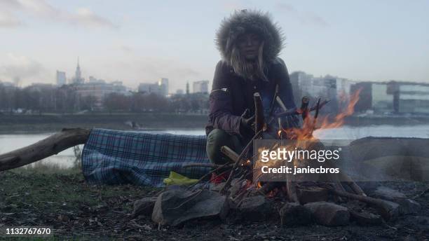 lone woman burning campfire on a riverside - homeless winter stock pictures, royalty-free photos & images