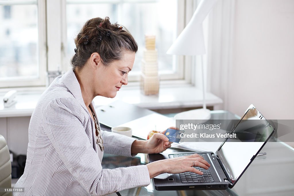 Mature woman holding credit card and using laptop