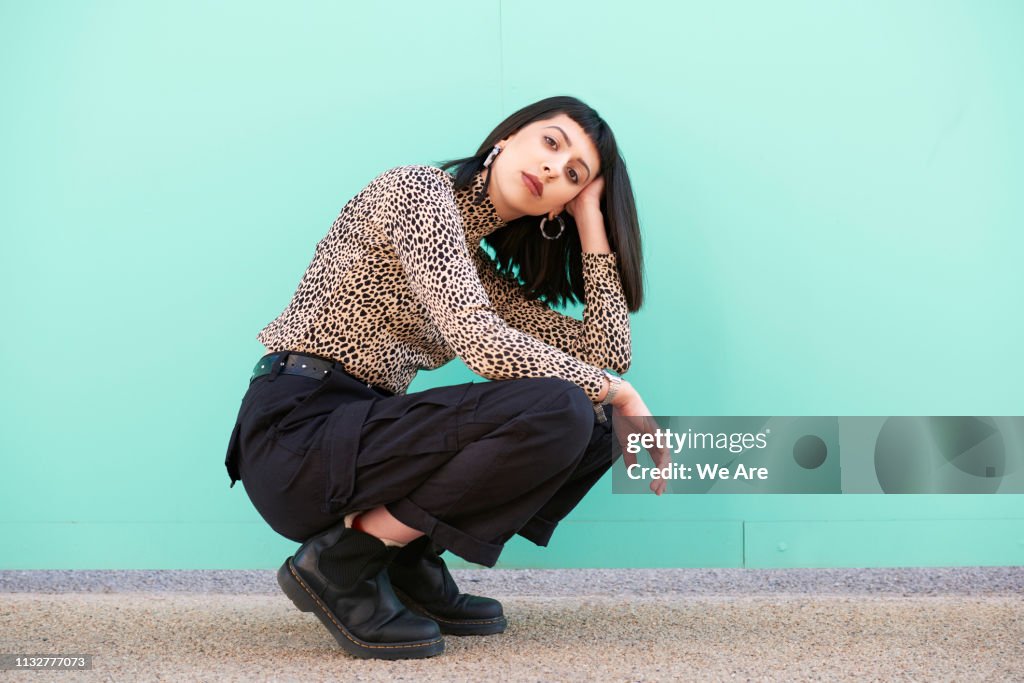 Young woman crouching down in front of blue wall.