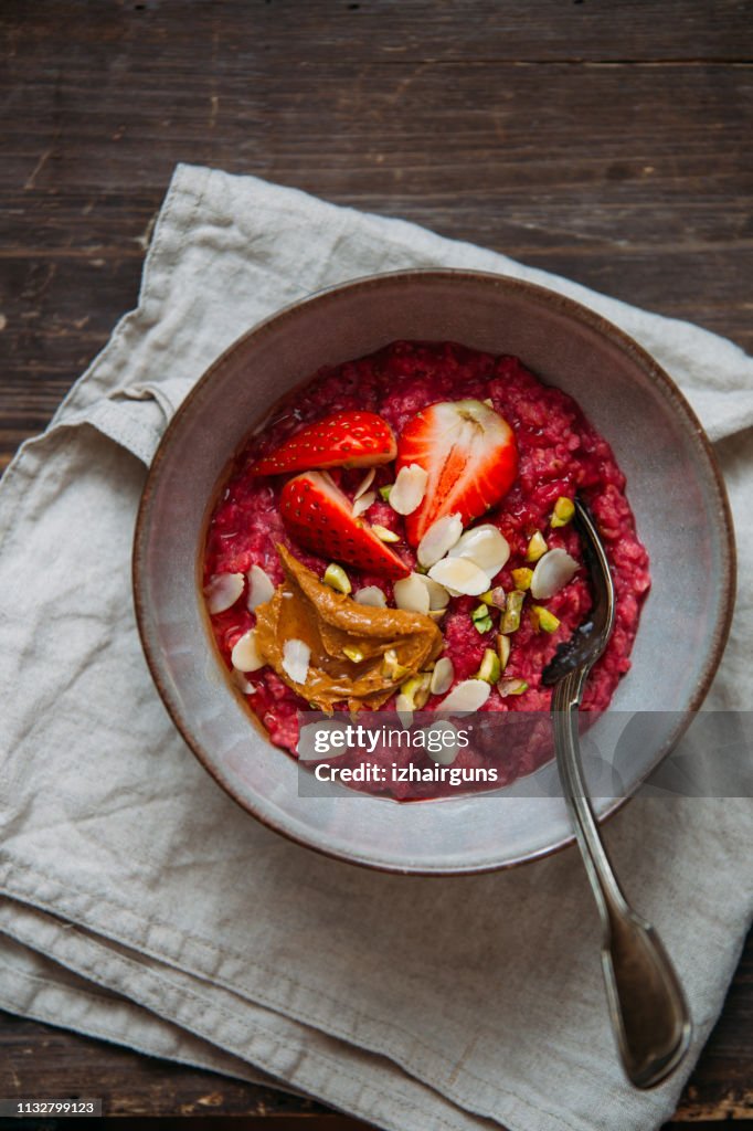 Oatmeal porridge with strawberries and fruit yogurt and pistachios, peanut butter and almond in bowl. Morning concept with copy space