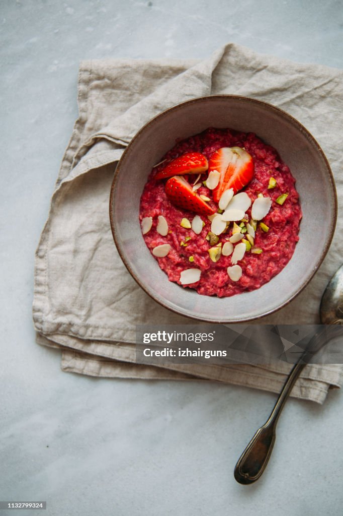 Oatmeal porridge with strawberries and fruit yogurt and pistachios, peanut butter and almond in bowl. Morning concept with copy space
