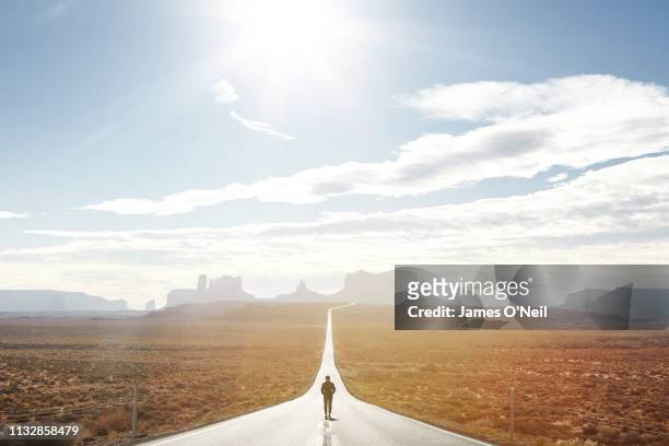 Lone traveller walking down empty road towards distant cliffs