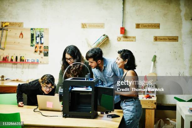 engineers examining plans on laptop while prototyping parts for project on 3d printer in workshop - stampante 3d foto e immagini stock