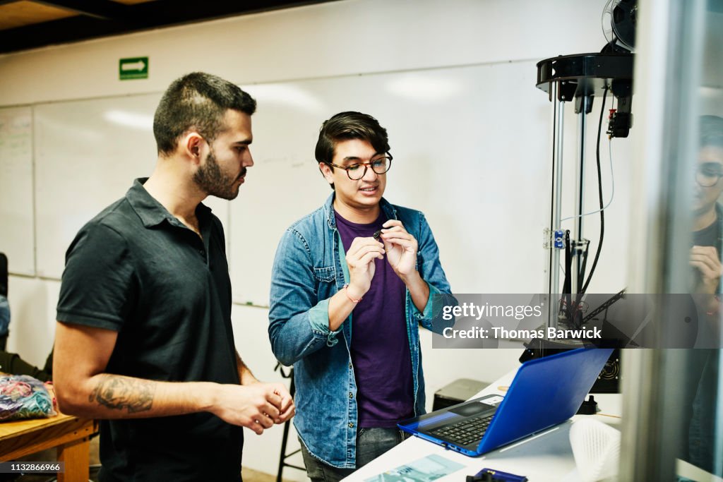 Engineers in discussion while prototyping part on 3D printer in design studio