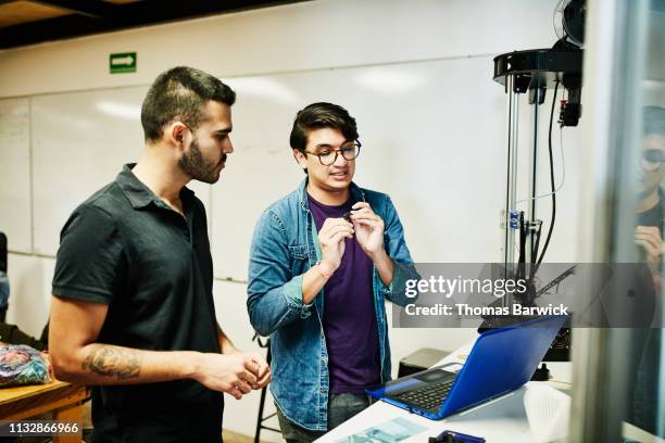 Engineers in discussion while prototyping part on 3D printer in design studio