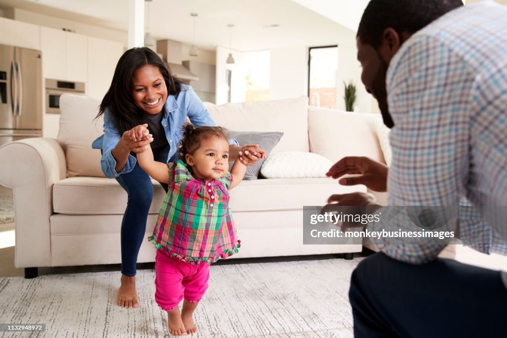 Family At Home Encouraging Baby Daughter To Take First Steps