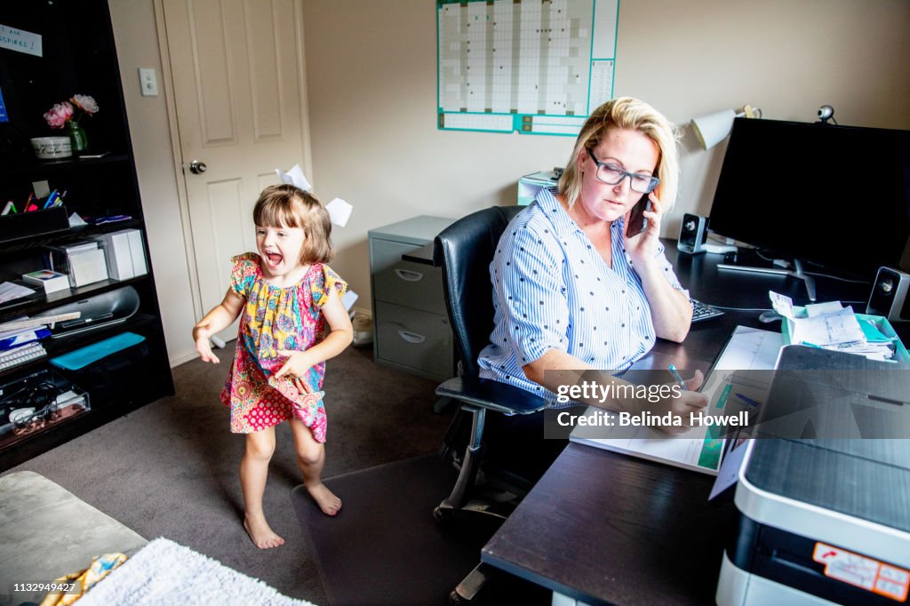 Middle Aged Women working from home in office whilst also looking after her young daugther.