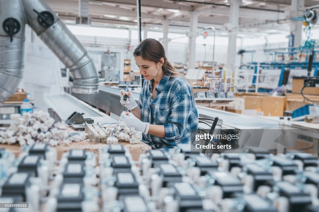 Industrial worker woman soldering cables of manufacturing equipment in a factory