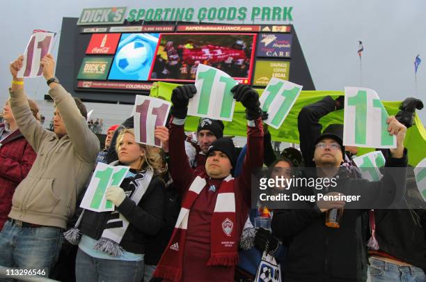 Fans hold up cards with the in burgundy and green during the 11th minute of action between the Colorado Rapids and the Chicago Fire at Dick's...