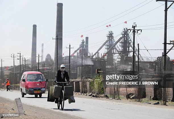 China-commodities-mining-environment by Allison JacksonA cyclist wears a protective face mask while riding along a dusty roadv where dozens of...