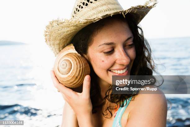 woman listening to seashell on beach - interested listener stock-fotos und bilder