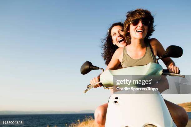 smiling women riding scooter on beach - woman riding scooter stock pictures, royalty-free photos & images