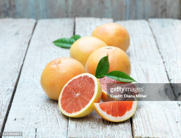 whole and half pink grapefruit on whitewashed wooden table - toronja - fotografias e filmes do acervo