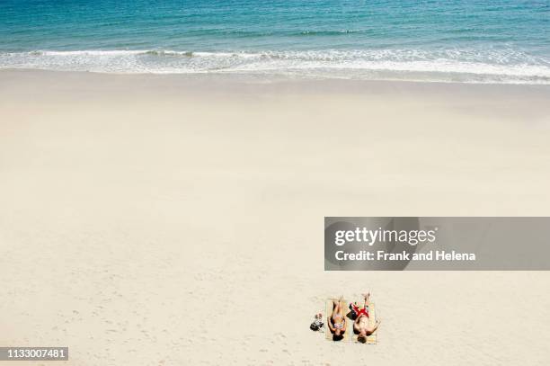 couple sunbathing on white sandy beach - couché de soleil photos et images de collection