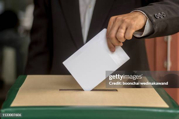 hand of a person casting a vote into the ballot box during elections - election foto e immagini stock