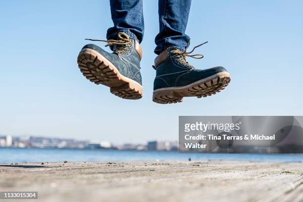 low section of man jumping on pier on sunny day in germany. - riemenschuh stockfoto's en -beelden