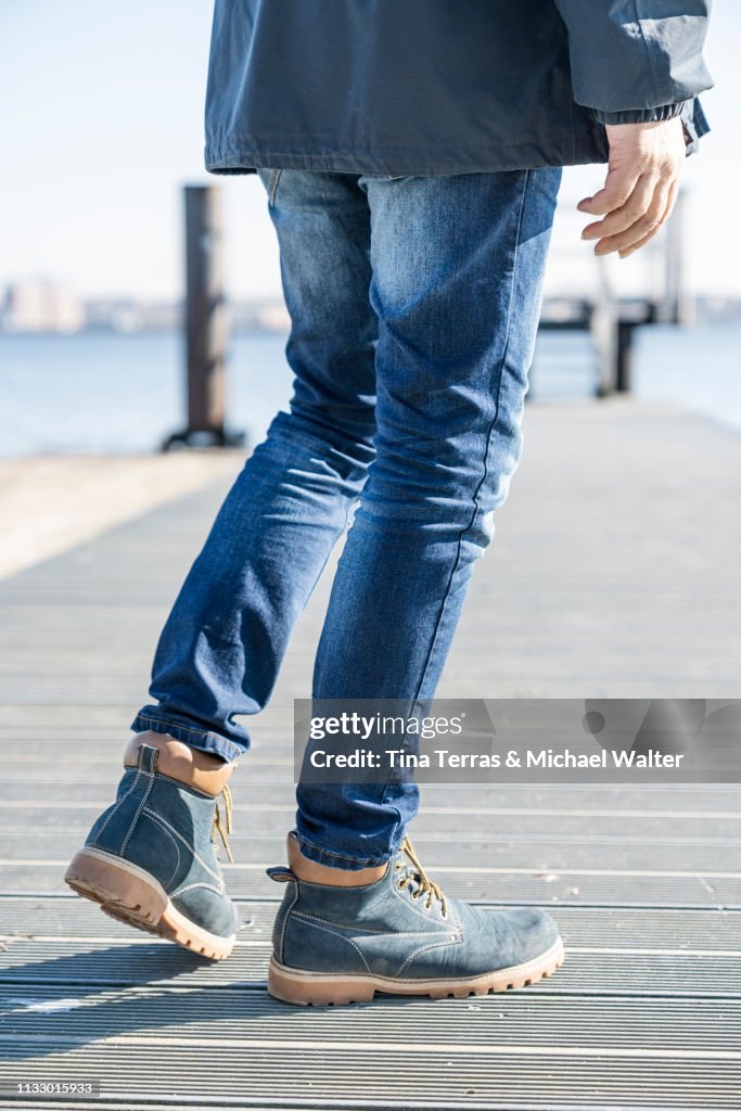 Low section of man walking on pier on sunny day in Germany.