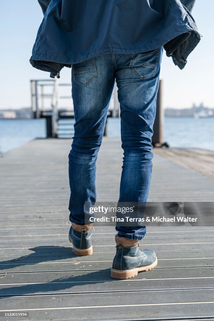 Low section of man walking on pier on sunny day in Germany.