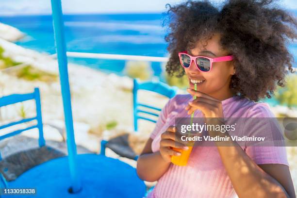 afro woman enjoying summer vacations and drinking juice - woman drinking juice stock pictures, royalty-free photos & images