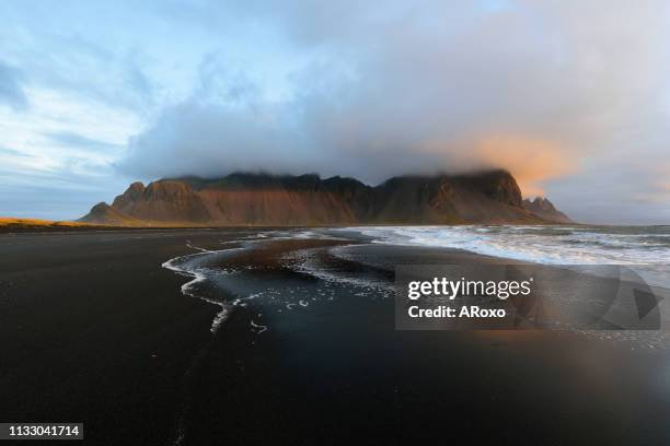 magical landscape of vestrahorn mountains and black sand dunes in iceland at sunrise.  panoramic view of the stokksnes headland in a colorful seascape. - black sand iceland stock-fotos und bilder