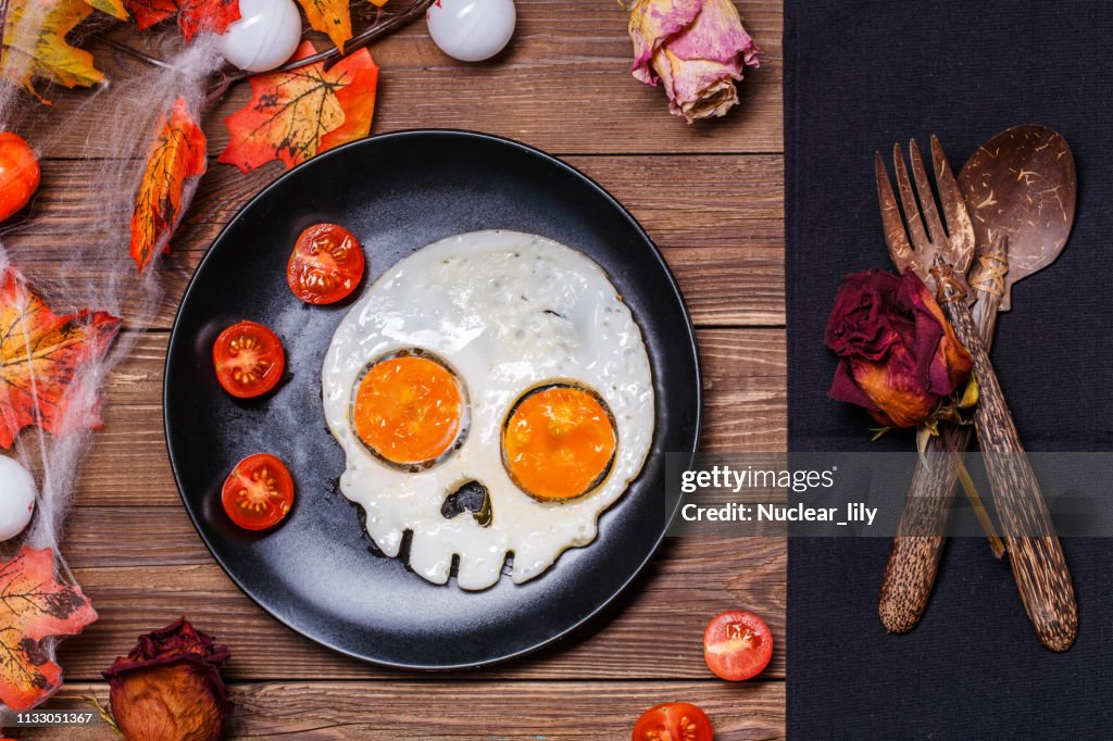 Fried eggs in the shape of a skull and fresh tomatoes. Breakfast in Halloween decorations.