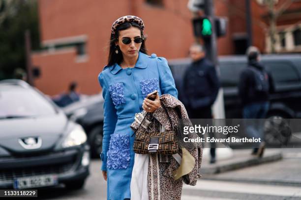 Gabriella Berdugo wears a leopard print headband, sunglasses, earrings, a blue tunic with pockets decorated with blue textile flowers, a Fendi bag, a...