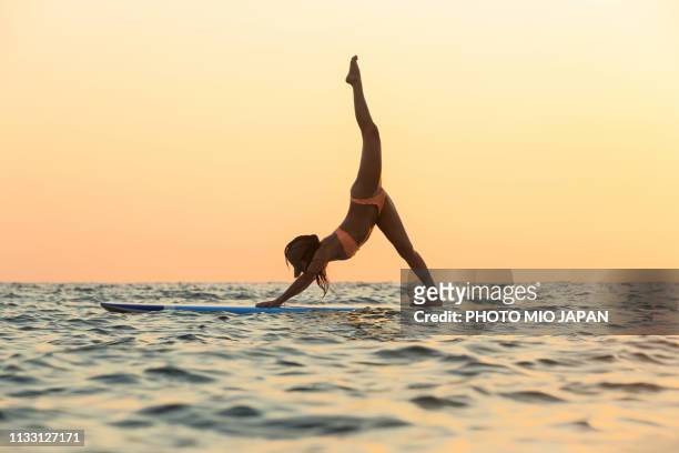 a young woman is doing sup yoga on the paddle board at the ocean. - practioners enjoy serenity of paddleboard yoga stockfoto's en -beelden