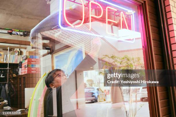 male business owner opening surfboard shop and turning on neon open sign in shop window. - butiksinvigning bildbanksfoton och bilder