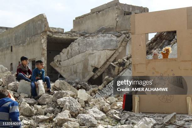 Children watch a puppet show performed by a Syrian actor, through a makeshift puppet theatre set up among the rubble of collapsed buildings in the...