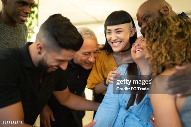 medewerkers omarmen een speciale behoeften ondernemer op de werkplek - gelijkwaardige behandeling stockfoto's en -beelden