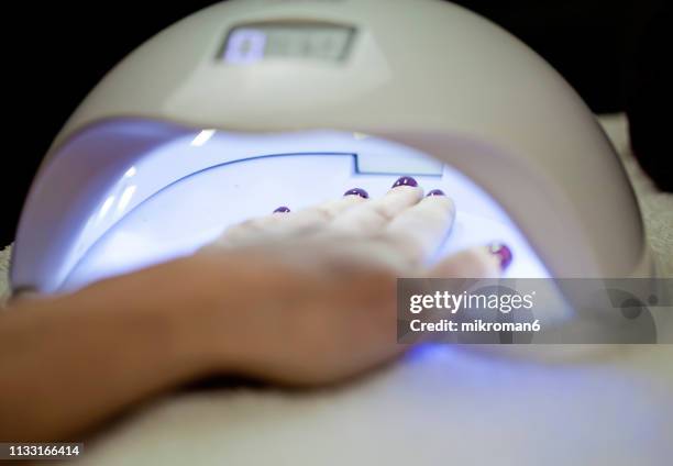 woman fliling nails with uv lamp in background. - get manicure stock-fotos und bilder