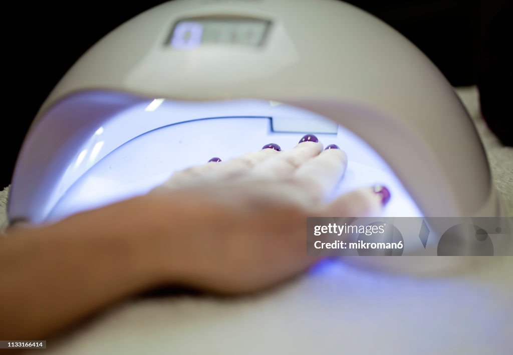 Woman Fliling Nails With UV Lamp in Background.