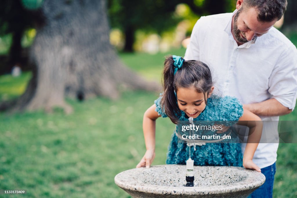 Father helping daughter to drink water in the park