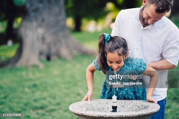 father helping daughter to drink water in the park - drinking fountain stock pictures, royalty-free photos & images