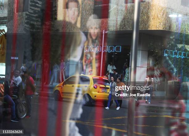 People are seen reflected in a window as they pass through the streets of a shopping district as the city deals with the influx of Venezuelans that...